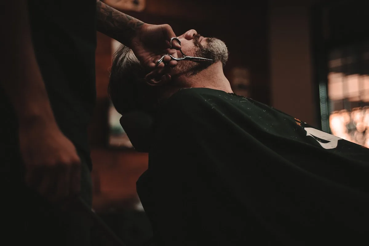A stylist giving a close hot-towel shave under soft lighting