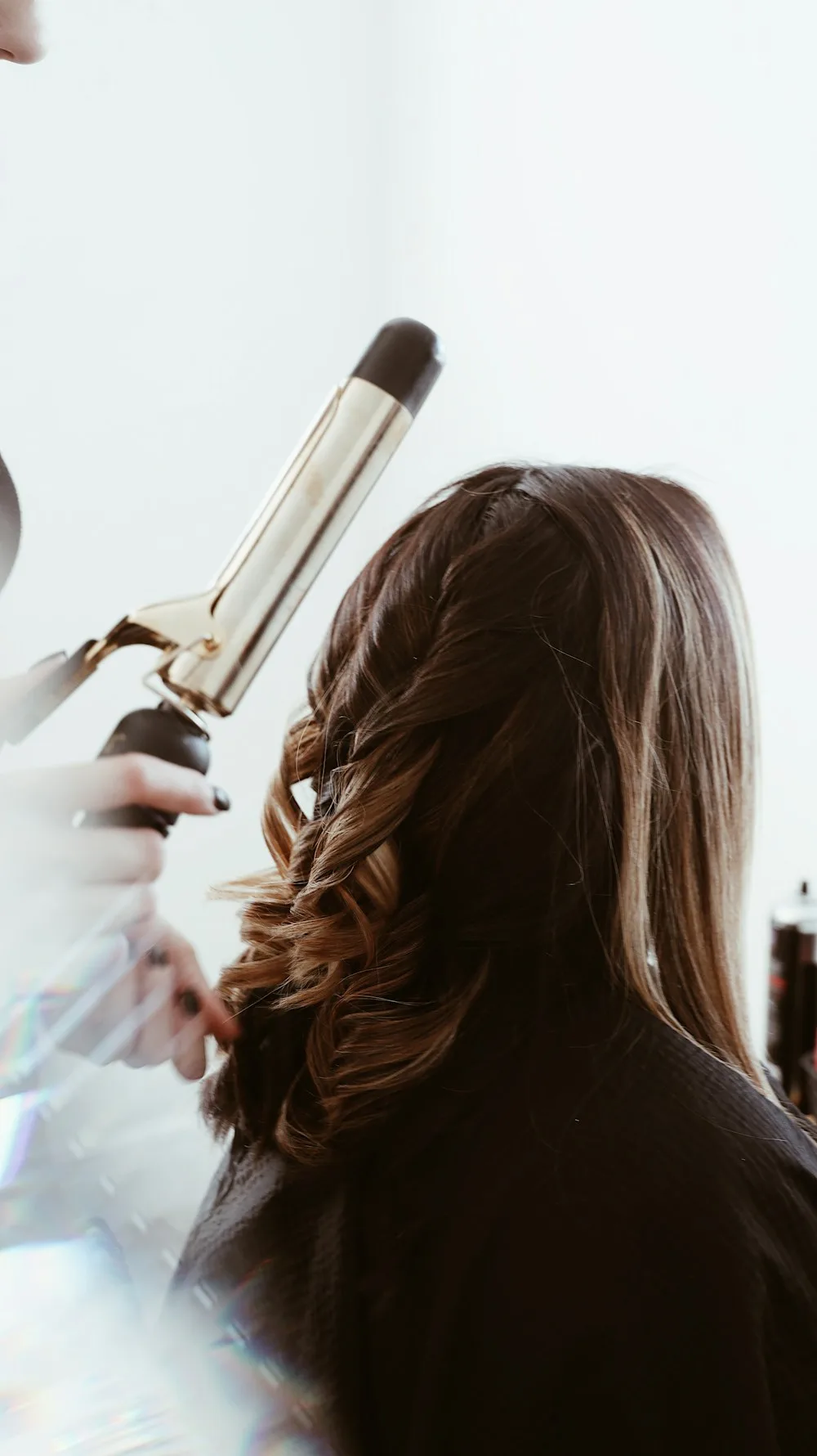 A stylist curling long hair with a gold styling iron